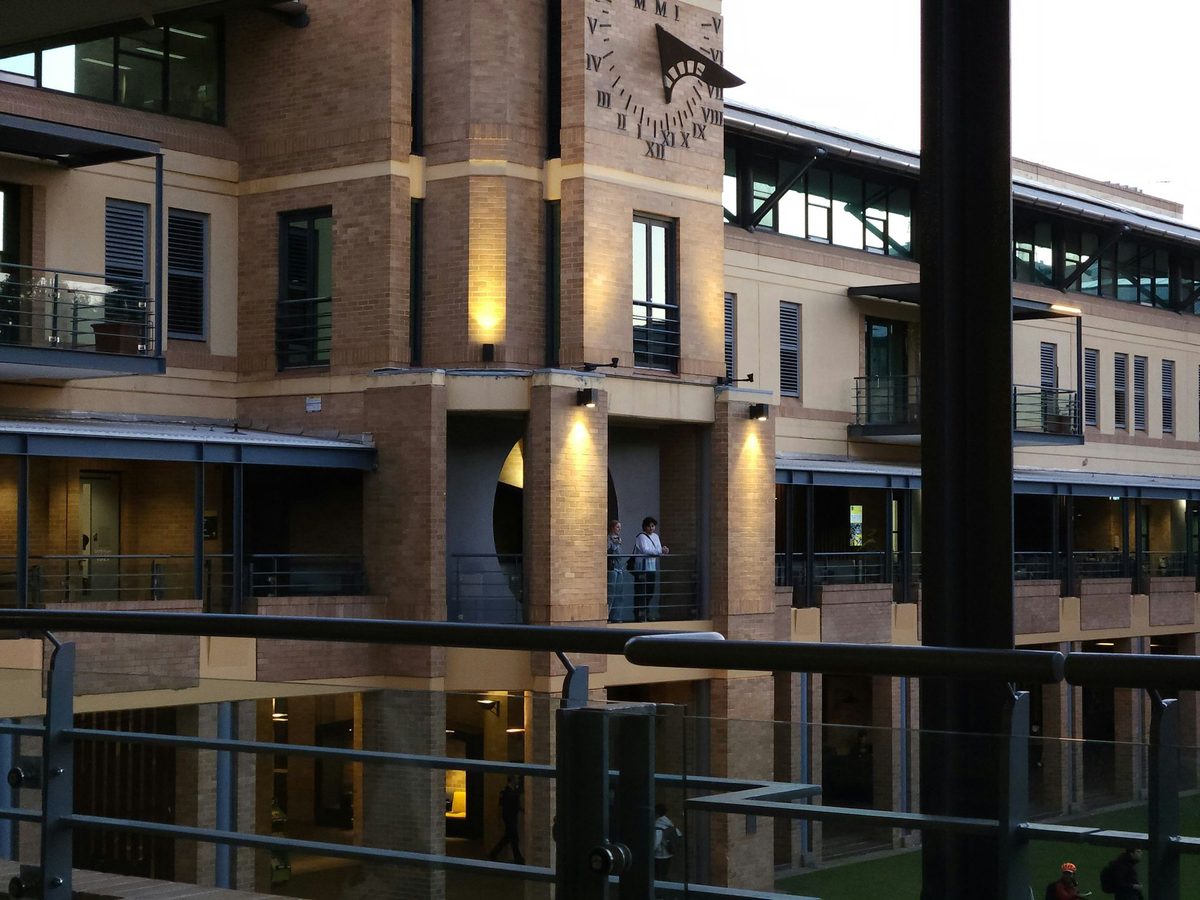 A brick clock tower with Roman numerals, lit warmly as evening comes